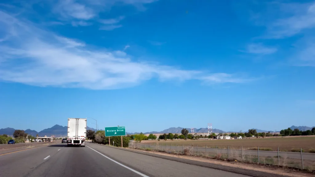 Highway scene with a truck, exit sign, and mountains under a blue sky.