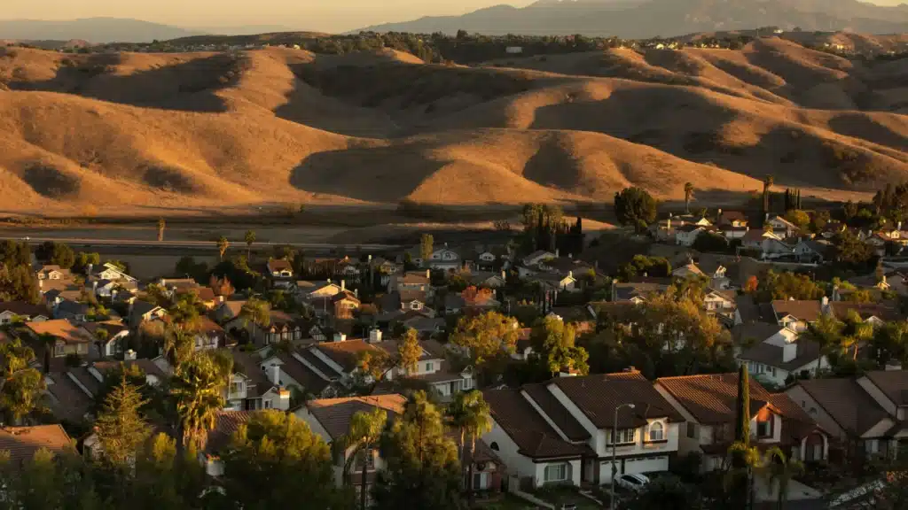 Aerial view of suburban homes with rolling hills and mountains at sunset.