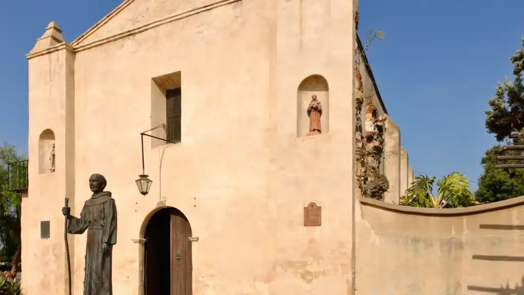 Historic mission-style church with a statue at the entrance under a clear blue sky.