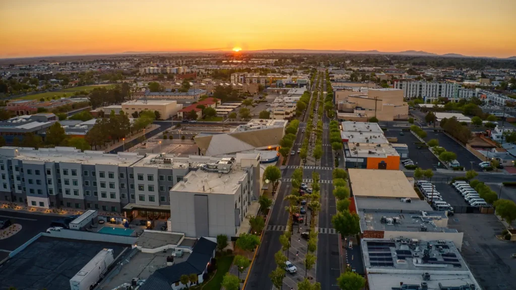 Wide aerial view of a suburban cityscape with streets, buildings, and parks in the evening light.